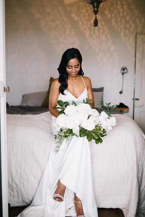 Bride sitting on bed with flower bouquet / Byron Bay