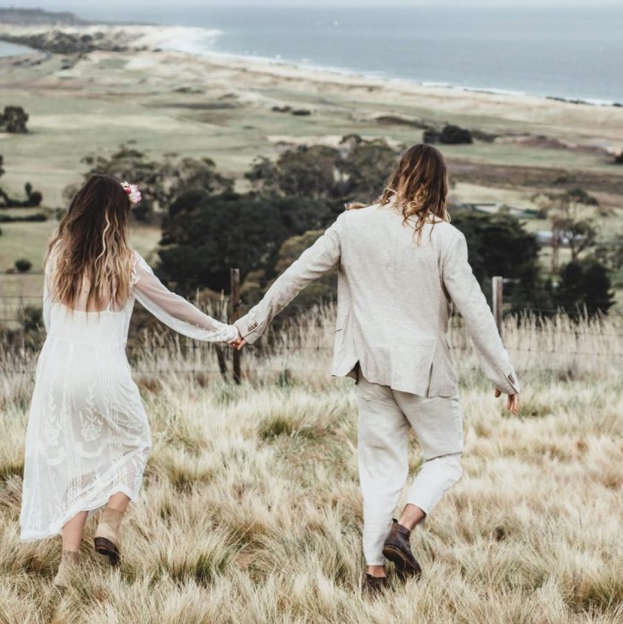 Bride and groom holding hands in Tasmanian countryside.